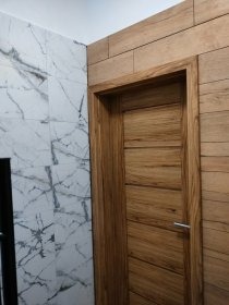 Wykończenie łazienki: drewnopodobna okładzina ścienna, drzwi z naturalnego drewna, marmurowe płytki. Nowoczesny design i dbałość o detale.