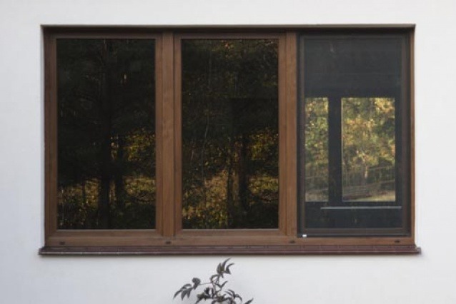 Drewniane okno z roletą dzień noc w Dobczycach. Widok na jesienny ogród przez szyby. Roleta opuszczona, zasłania część okna. Minimalistyczny design.