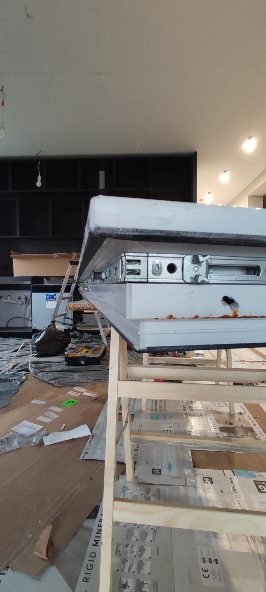 Montaż okna PCV: widok z bliska na mechanizm okna umieszczonego na drewnianym stelażu w surowym wnętrzu, narzędzia w tle. Etap instalacji.