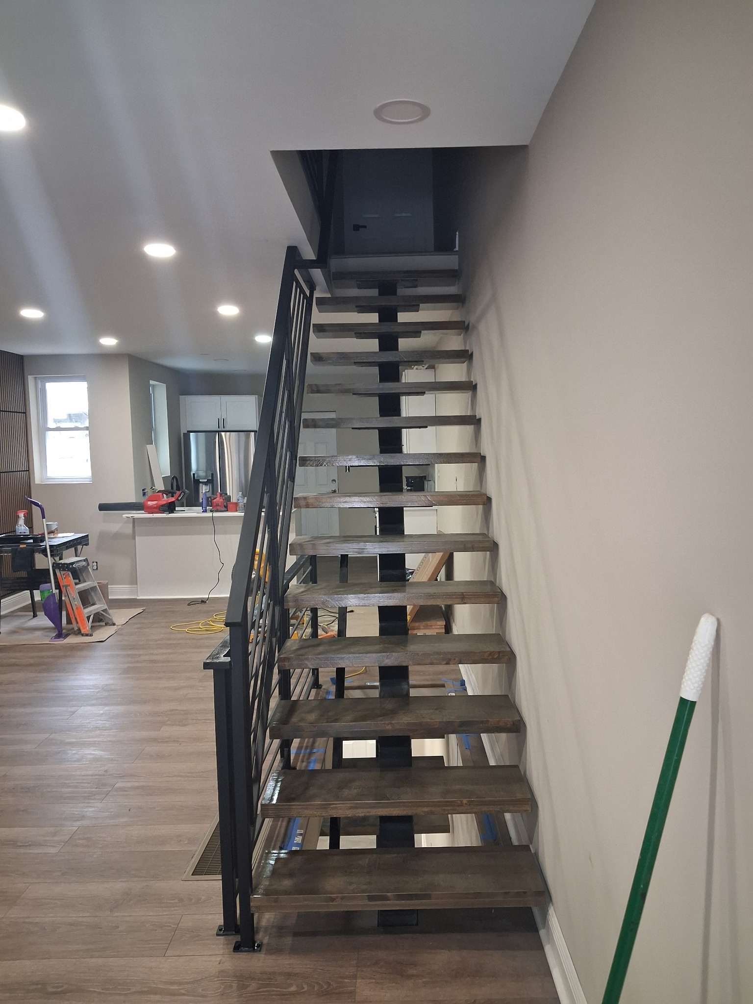 Nowoczesne schody metalowe z drewnianymi stopniami w jasnym wnętrzu domu. Minimalistyczny design balustrady. Widok z dołu na górę, oświetlenie sufitowe.