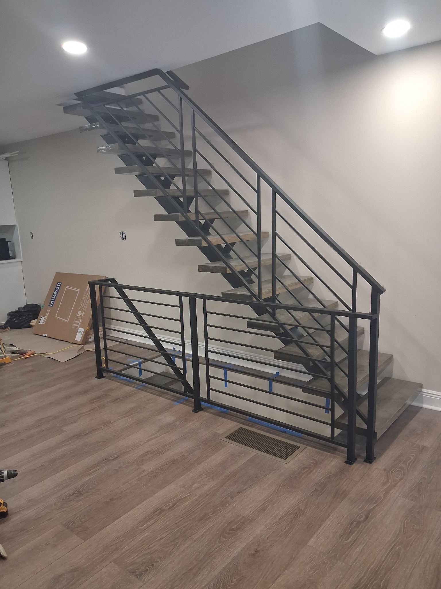 Nowoczesne schody metalowe z czarną balustradą w jasnym wnętrzu. Widoczne narzędzia i karton sugerują trwający montaż.