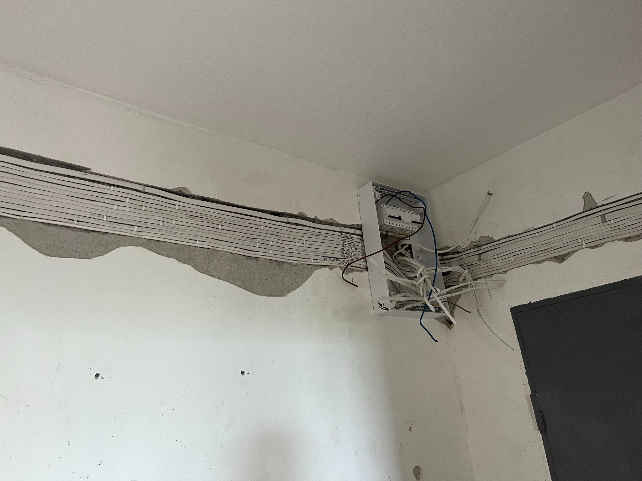 Rozprowadzenie przewodów elektrycznych w korytach ściennych, skrzynka rozdzielcza z widocznymi przewodami. Ściany w trakcie wykończenia.