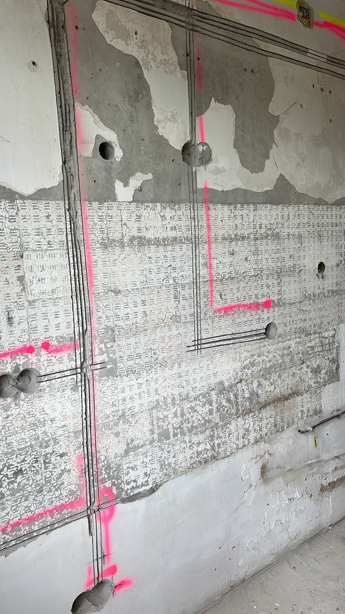 Ściana w trakcie remontu z widoczną instalacją elektryczną, zaznaczoną różowym sprayem. Widoczne kable, puszki instalacyjne i fragmenty starej tapety.