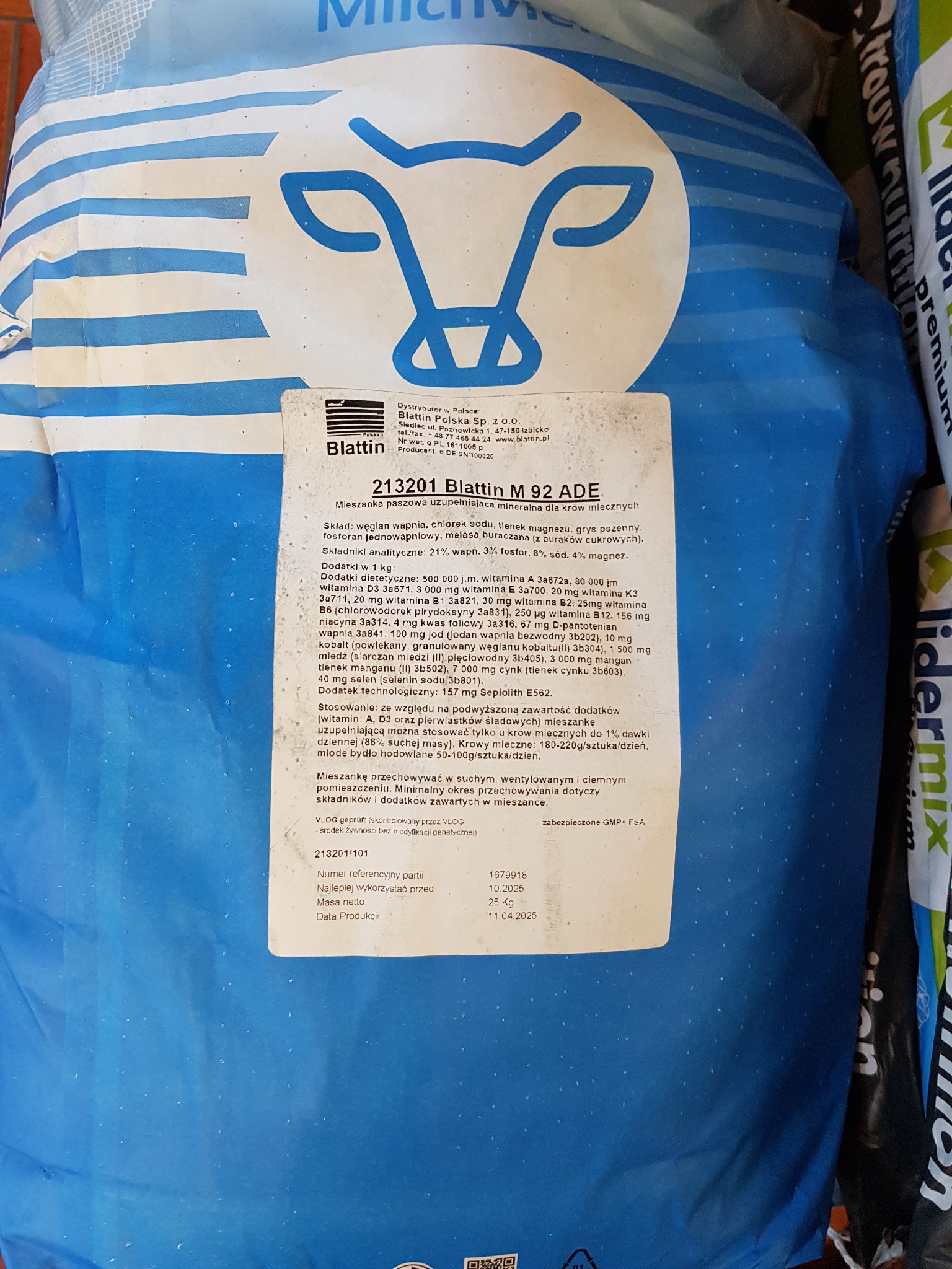 Worek paszowy z mieszanką uzupełniającą dla krów mlecznych Blattin M 92 ADE. Widoczny skład, dawkowanie i data ważności. Opakowanie w kolorze białym i niebieskim.
