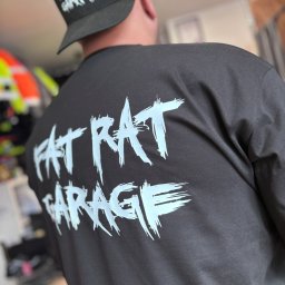 MAKT WIKTOR JAKUBOWSKI - Czarna koszulka i czapka z białym nadrukiem 'FAT RAT GARAGE', widok z tyłu na osobie. Grafika w stylu graffiti. Elementy garderoby z nadrukiem.