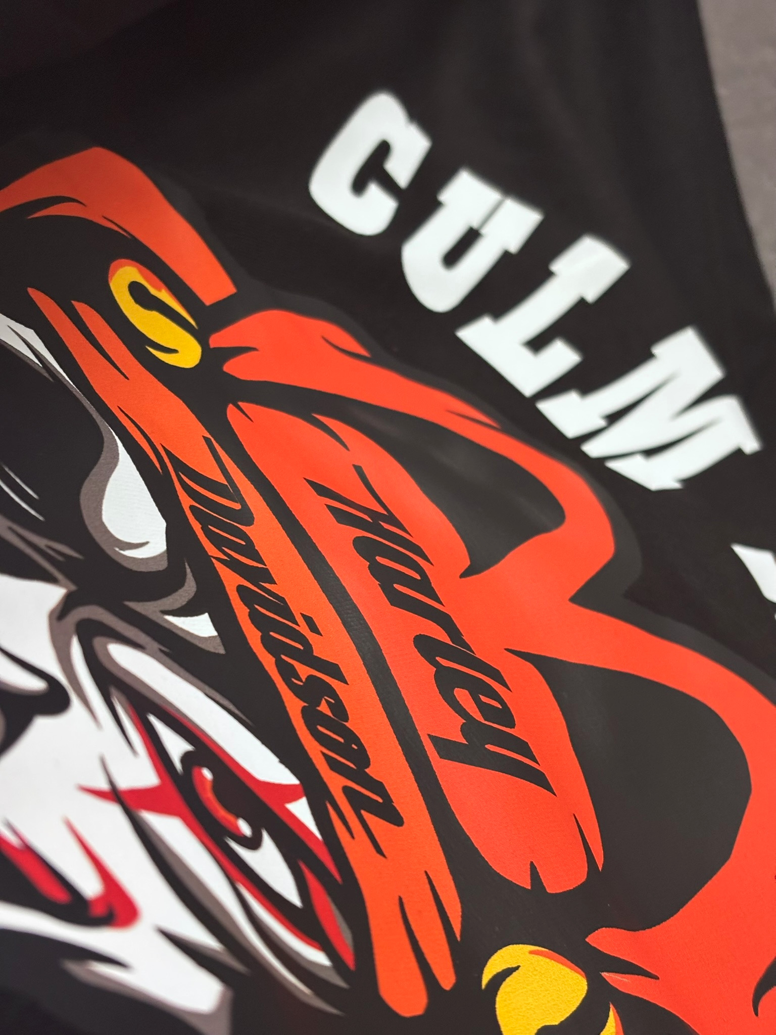 Czarna koszulka z nadrukiem w odcieniach czerwieni, bieli i żółci, przedstawiającym motyw wilka z napisem 'Harley Davidson'. Ujęcie z bliska, lekko pod kątem.