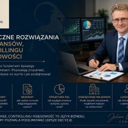 Julian Wielądek - consulting - Uśmiechnięty konsultant w garniturze pisze na dokumencie z wykresami, siedząc przy biurku z laptopem i dwoma monitorami prezentującymi dane finansowe i controllingowe.