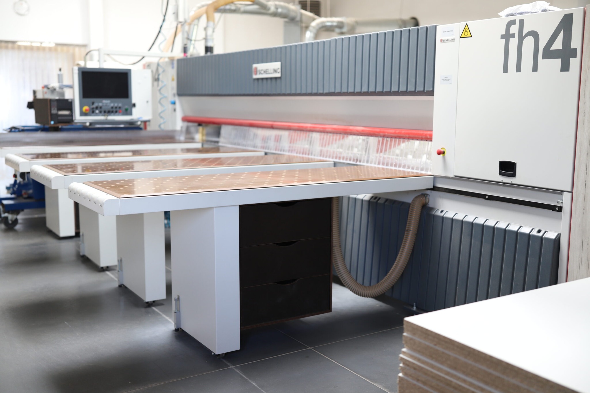 Profesjonalna piła panelowa Schelling fh4 z systemem podawania i odbioru płyt. Widoczny blat roboczy z otworami i stos płyt gotowych do obróbki.
