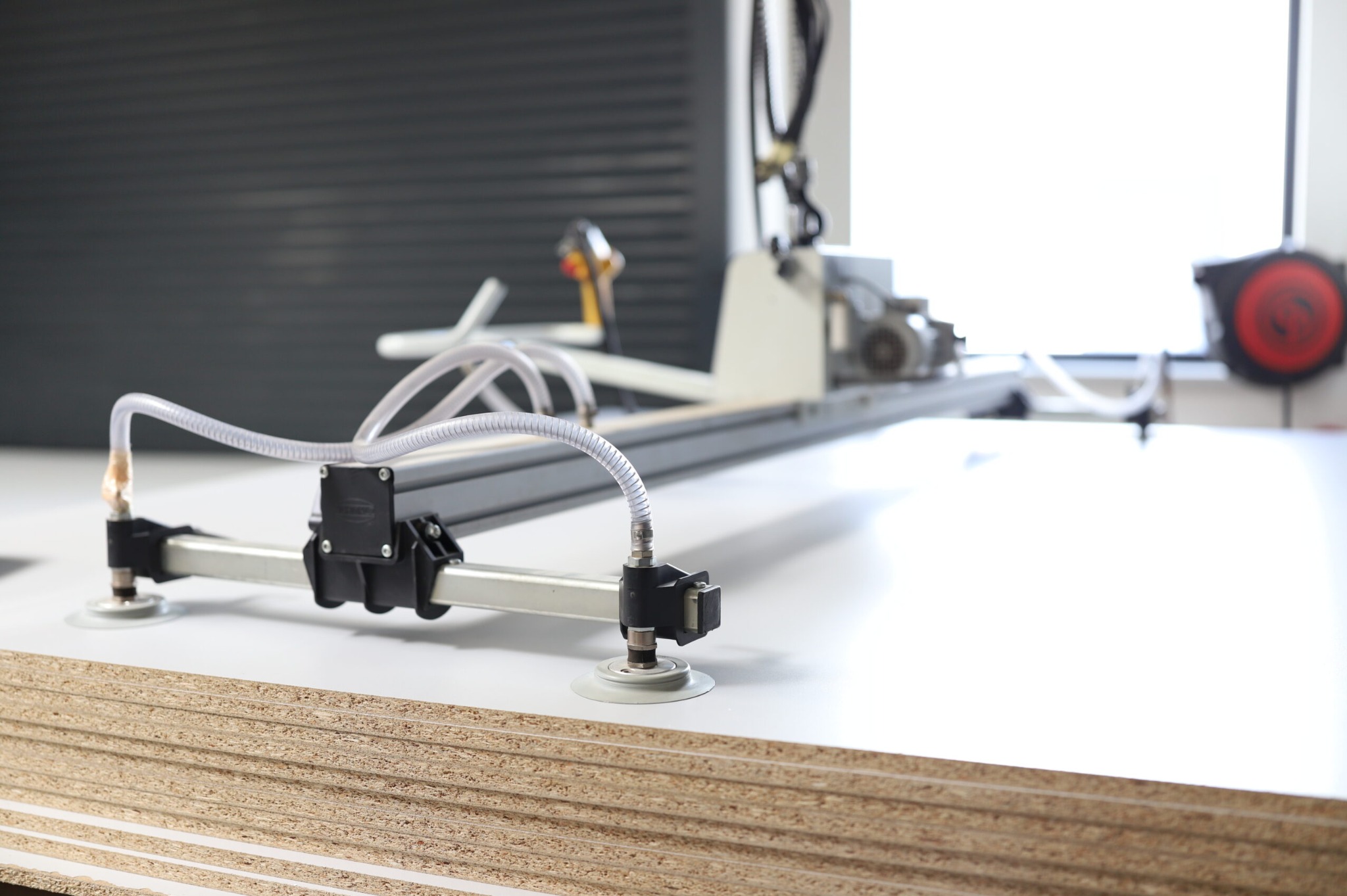 Specjalistyczna maszyna do obróbki płyt meblowych z przyssawkami, widoczna w warsztacie. Płyty ułożone w stos, przygotowane do pracy.