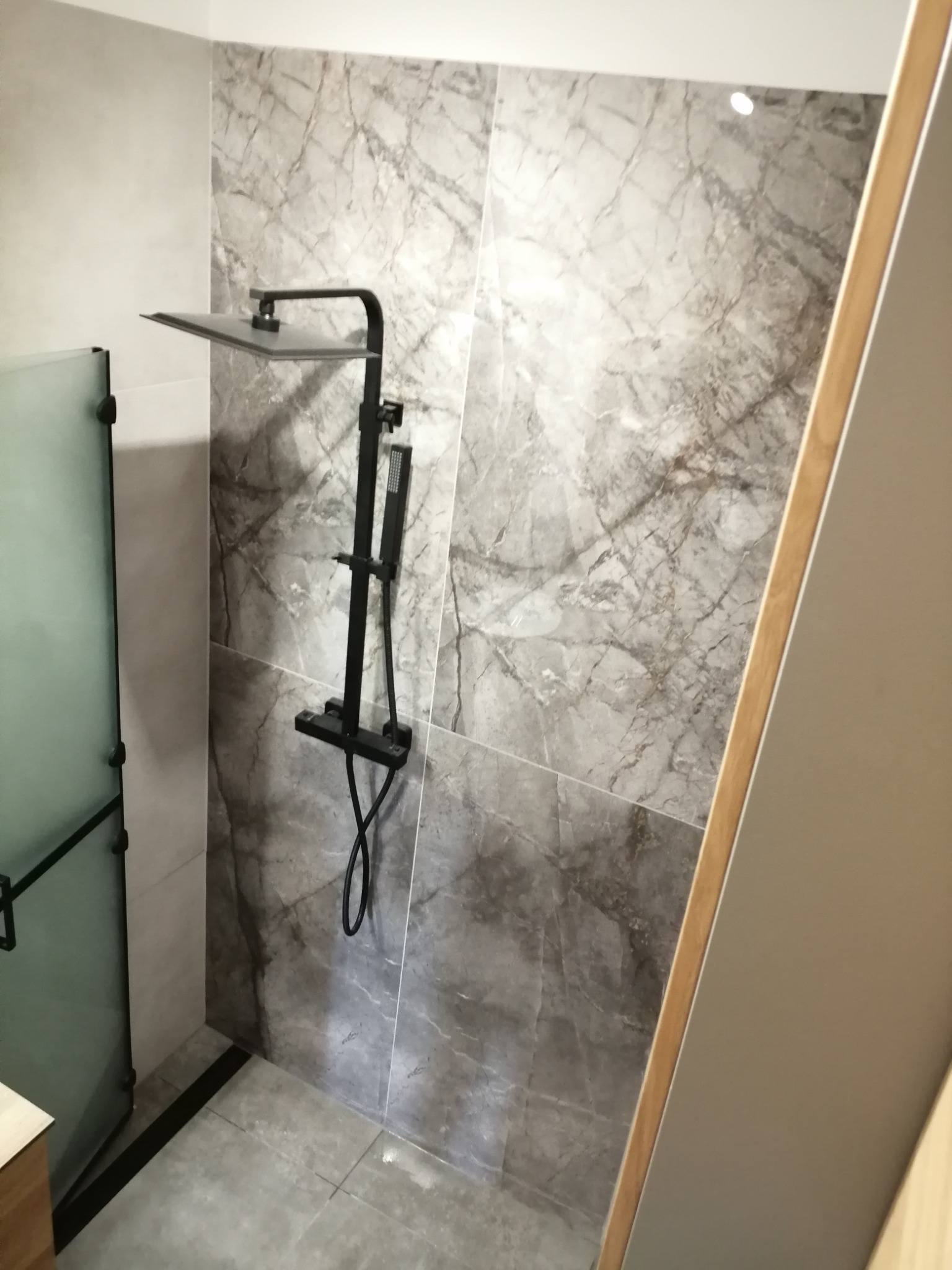 Wykończona kabina prysznicowa z czarną armaturą, marmurowe płytki na ścianach i szklane drzwi. Minimalistyczny design.