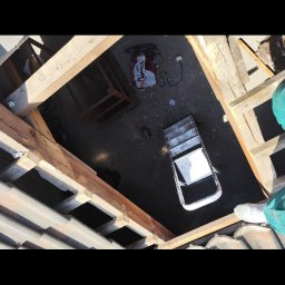 Firma Usługowo-remontowa IRENA - Widok z góry na rozłożony dach z odsłoniętą konstrukcją więźby, narzędzia pracy i drabinę. Fragment nogi w białym bucie widoczny w prawym dolnym rogu.