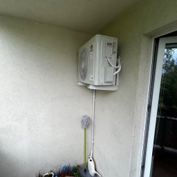 Peli-Cool klimatyzacja Dawid Bukowski - Klimatyzator marki Gree zamontowany na balkonie, z widoczną instalacją odprowadzającą skropliny. Obok rośliny w doniczce i mop. Widok z dołu na urządzenie.