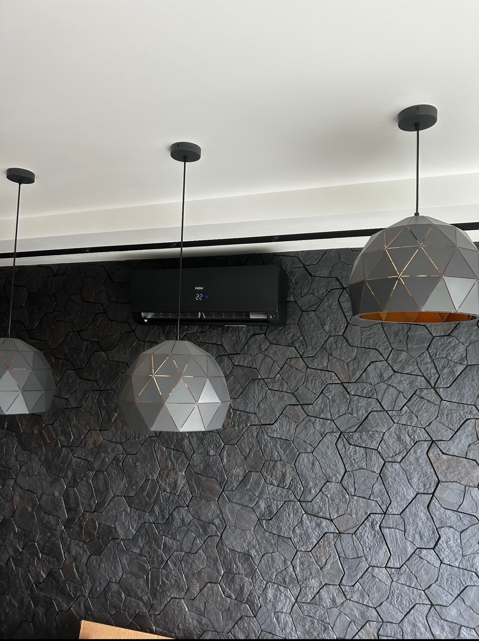 Czarna klimatyzacja Haier na ścianie z kamienia w Wykach. Geometryczne lampy wiszące. Nowoczesny design i komfort termiczny w jednym ujęciu.