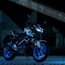 Biało-czarny motocykl Yamaha MT-15 z niebieskimi felgami, zaparkowany nocą pod wiaduktem z japońskimi napisami.