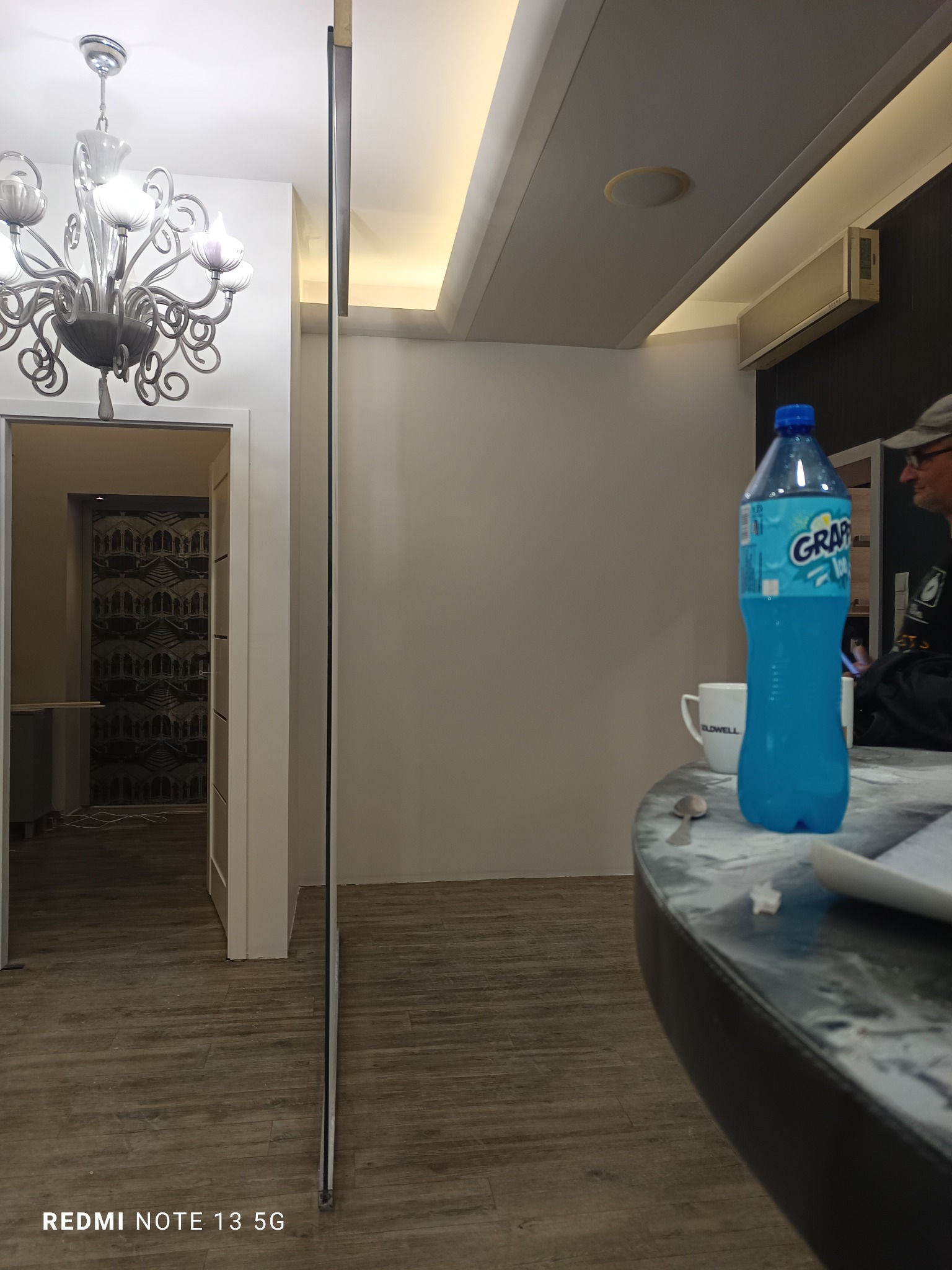 Wnętrze mieszkania po remoncie: parkiet, ściany w jasnych barwach, ozdobny żyrandol, widok na pokój z tapetą. Widoczne ślady po pracy na blacie.