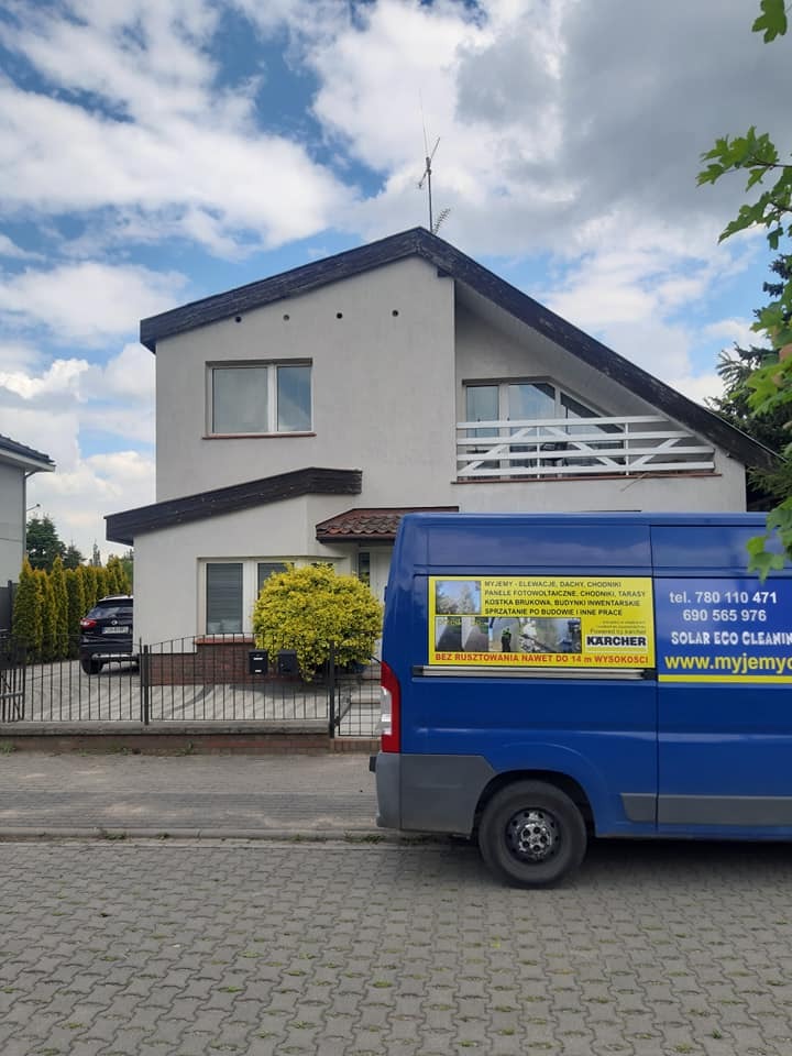 Dwupiętrowy dom z jasną elewacją i ciemnym dachem, na tle błękitnego nieba z chmurami. Obok zaparkowany niebieski bus z reklamą firmy czyszczącej.