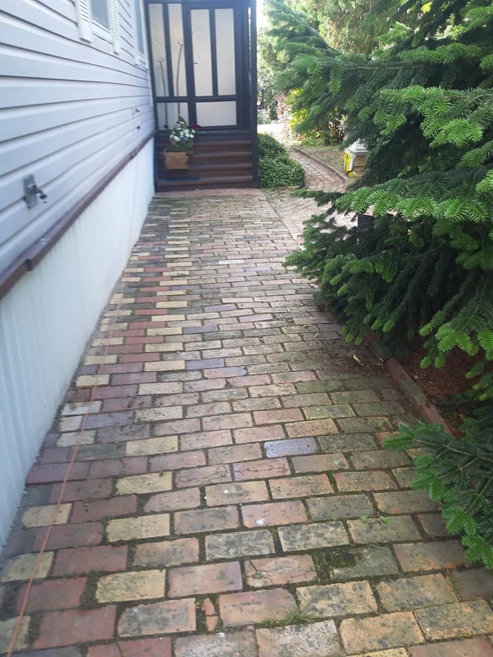 Zaniedbana, wielobarwna kostka brukowa prowadząca do wejścia domu z drewnianymi schodami. Widoczne zabrudzenia i mech na powierzchni kostki.