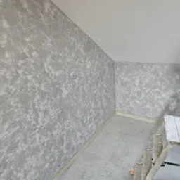 Pokój po szpachlowaniu z efektem dekoracyjnym na ścianach, widoczna drabina malarska, przygotowane gniazdko elektryczne i listwa przypodłogowa.