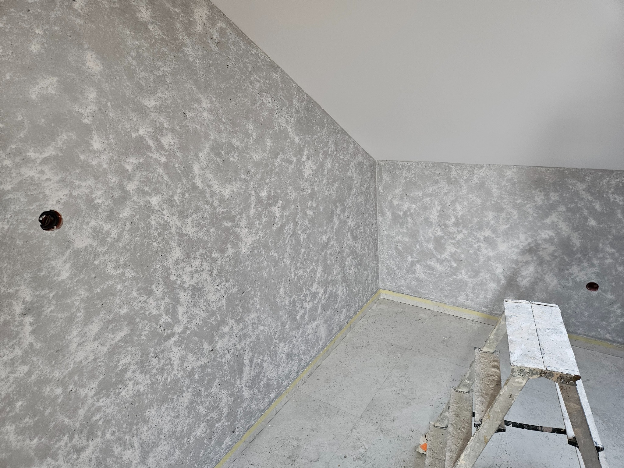 Pokój po szpachlowaniu z efektem dekoracyjnym na ścianach, widoczna drabina malarska, przygotowane gniazdko elektryczne i listwa przypodłogowa.