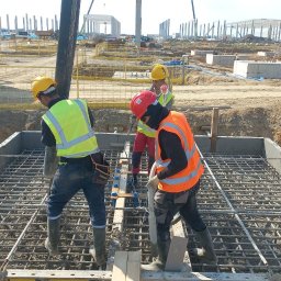 Merob Sp.z o.o. - Wylewanie betonu na zbrojenie fundamentu przez robotników w Sopot. Widoczny betonowóz i szkielet konstrukcji budynku w tle.