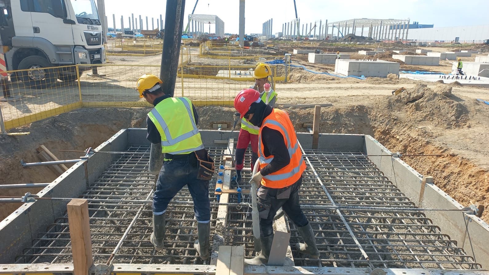 Wylewanie betonu na zbrojenie fundamentu przez robotników w Sopot. Widoczny betonowóz i szkielet konstrukcji budynku w tle.