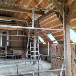 MATEUSZ ŻUKOWSKI - Poddasze z drewnianą konstrukcją i ociepleniem z wełny mineralnej, widoczne pakiety izolacyjne Steico flex, drabina i rusztowanie. W tle okna dachowe.