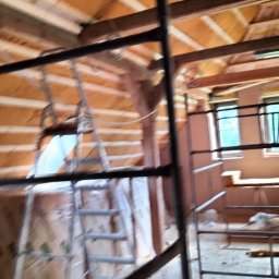 MATEUSZ ŻUKOWSKI - Poddasze w trakcie ocieplania z widocznymi belkami stropowymi, izolacją i rusztowaniem. Prace wykończeniowe wewnątrz budynku.