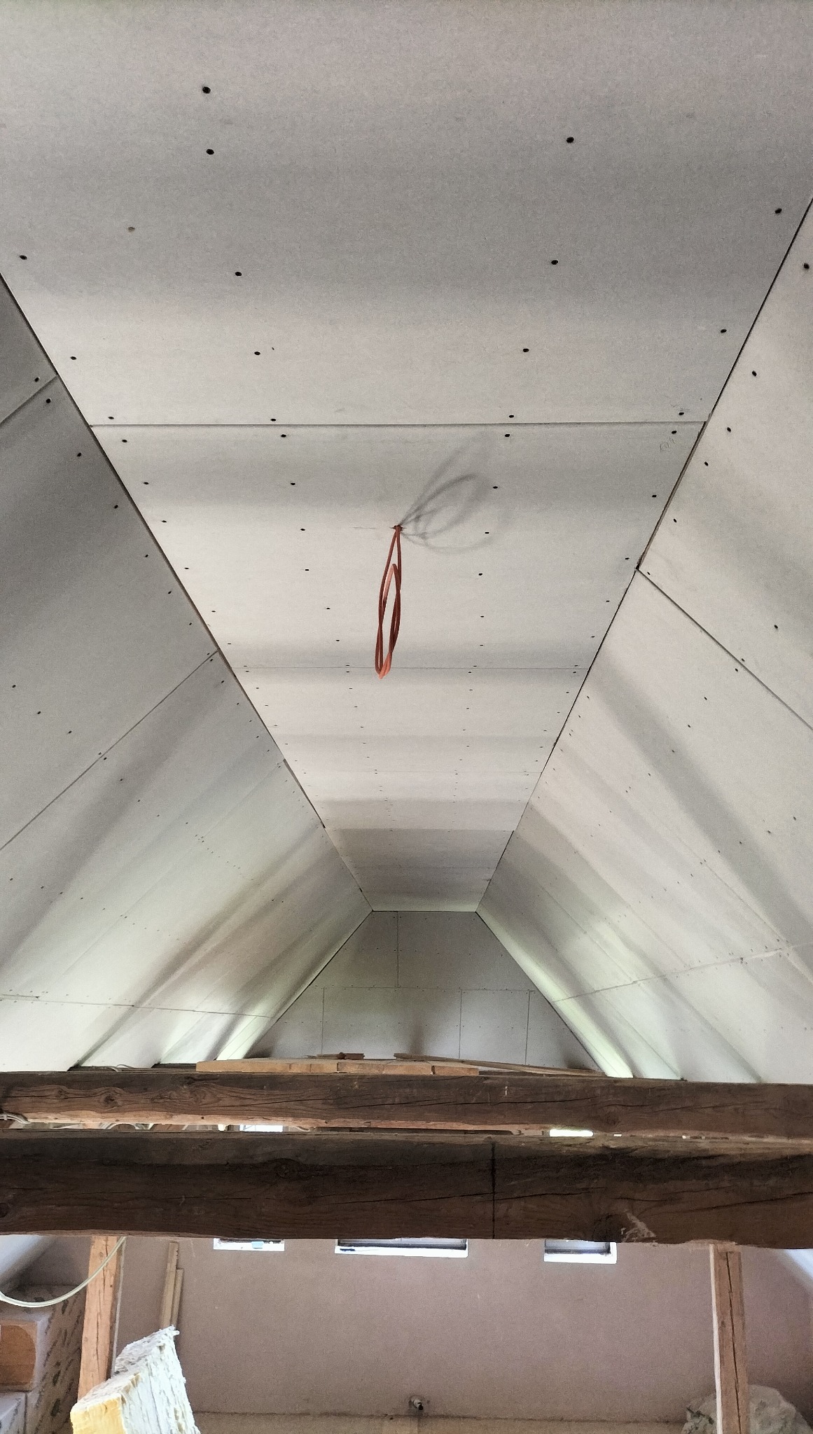 Płyty kartonowo-gipsowe zamontowane na skośnym poddaszu, widok z dołu, element drewnianej konstrukcji w dolnej części kadru, pomarańczowy kabel zwisa z sufitu.