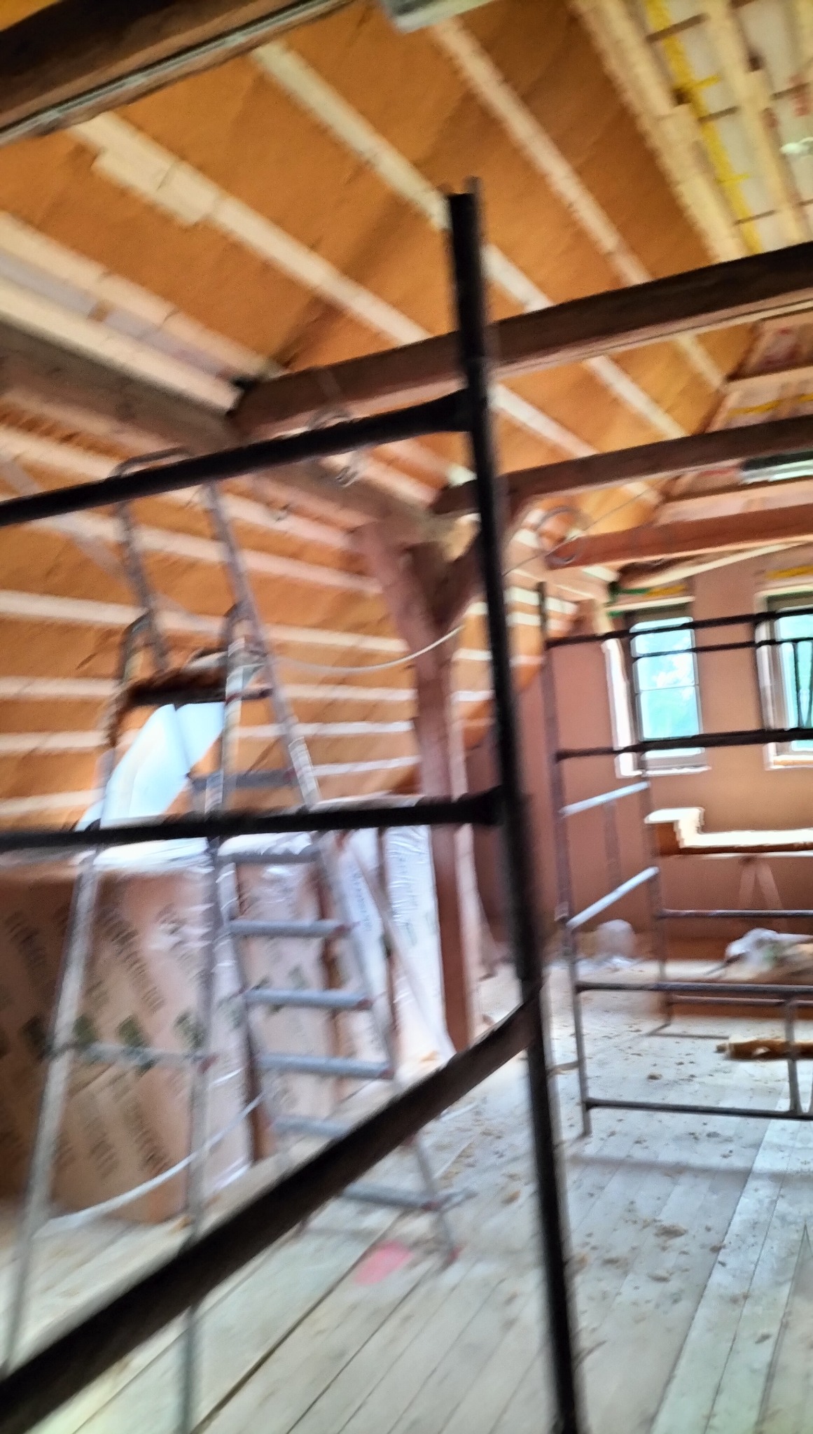 Poddasze w trakcie ocieplania z widocznymi belkami stropowymi, izolacją i rusztowaniem. Prace wykończeniowe wewnątrz budynku.