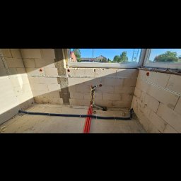 Paweł Bubeła Usługi Elektryczne - Surowy stan łazienki z instalacją elektryczną i hydrauliczną w trakcie montażu. Widoczne kable w korytkach i rury w ścianach z betonu komórkowego.