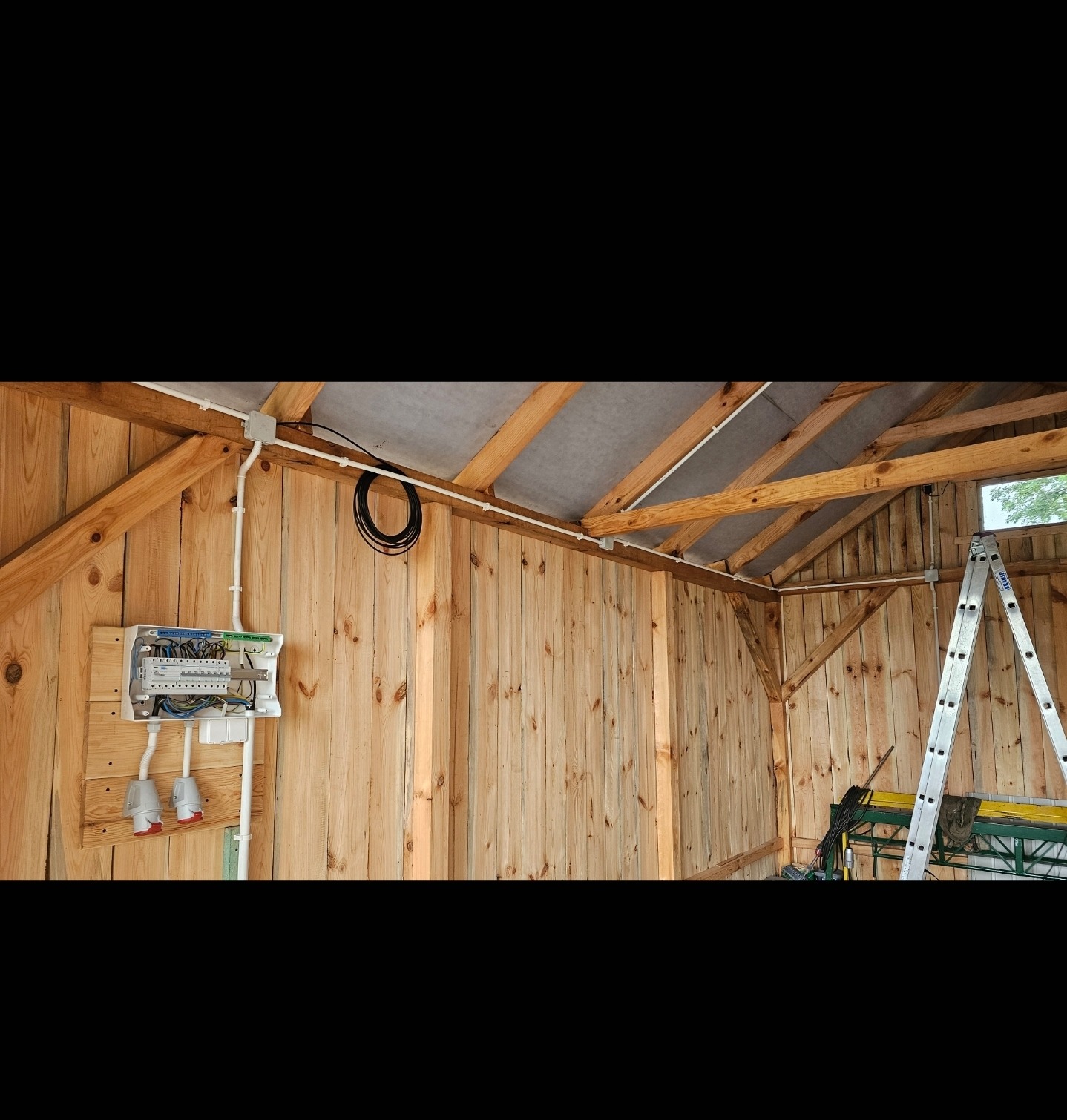 Rozdzielnia elektryczna z zabezpieczeniami i gniazdami siłowymi zamontowana na drewnianej ścianie wewnątrz budynku o konstrukcji szkieletowej.