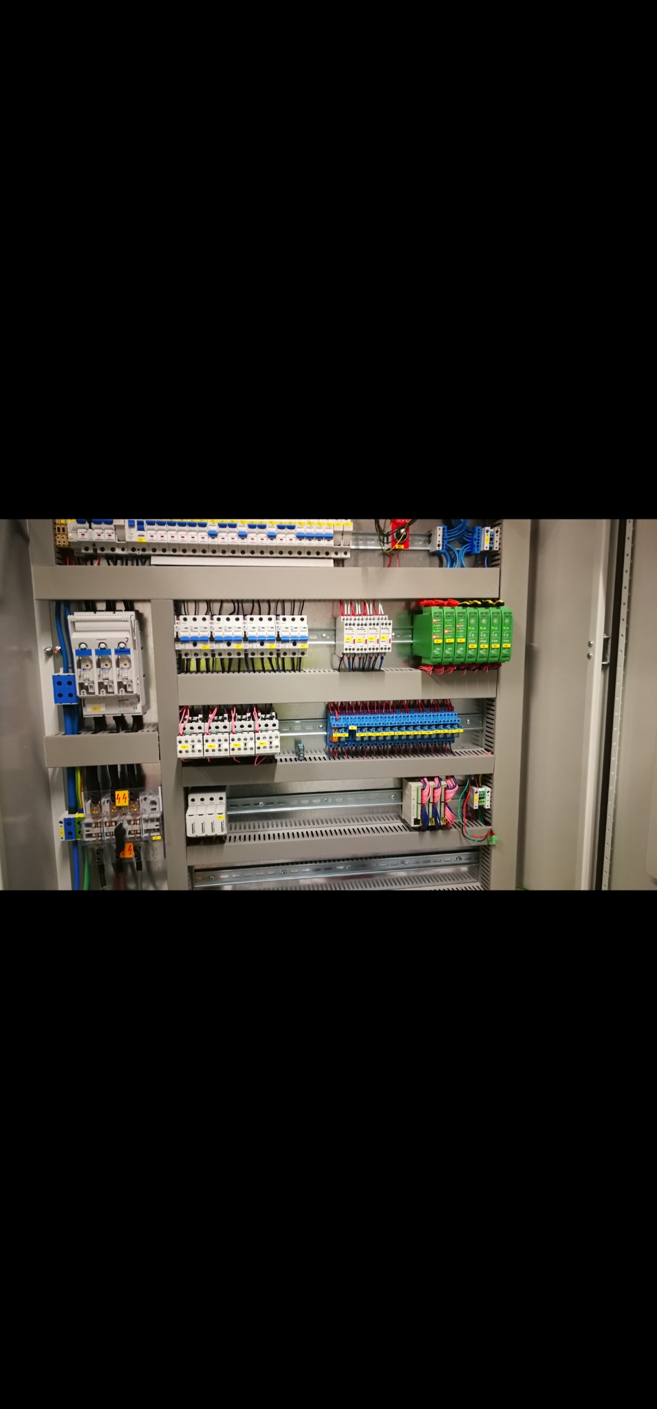 Rozdzielnica elektryczna z bezpiecznikami, stycznikami i przewodami wewnątrz szafy sterowniczej. Widoczne elementy instalacji elektrycznej w szarej obudowie.