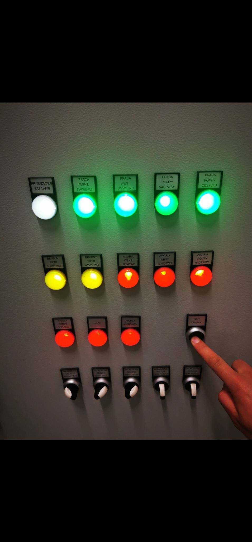 Panel sterowania z diodami sygnalizacyjnymi i przełącznikami, wciśnięty przycisk testu lampek. Widoczne opisy: 'Praca went. nawiewu', 'Awaria pompy nagrzew'.