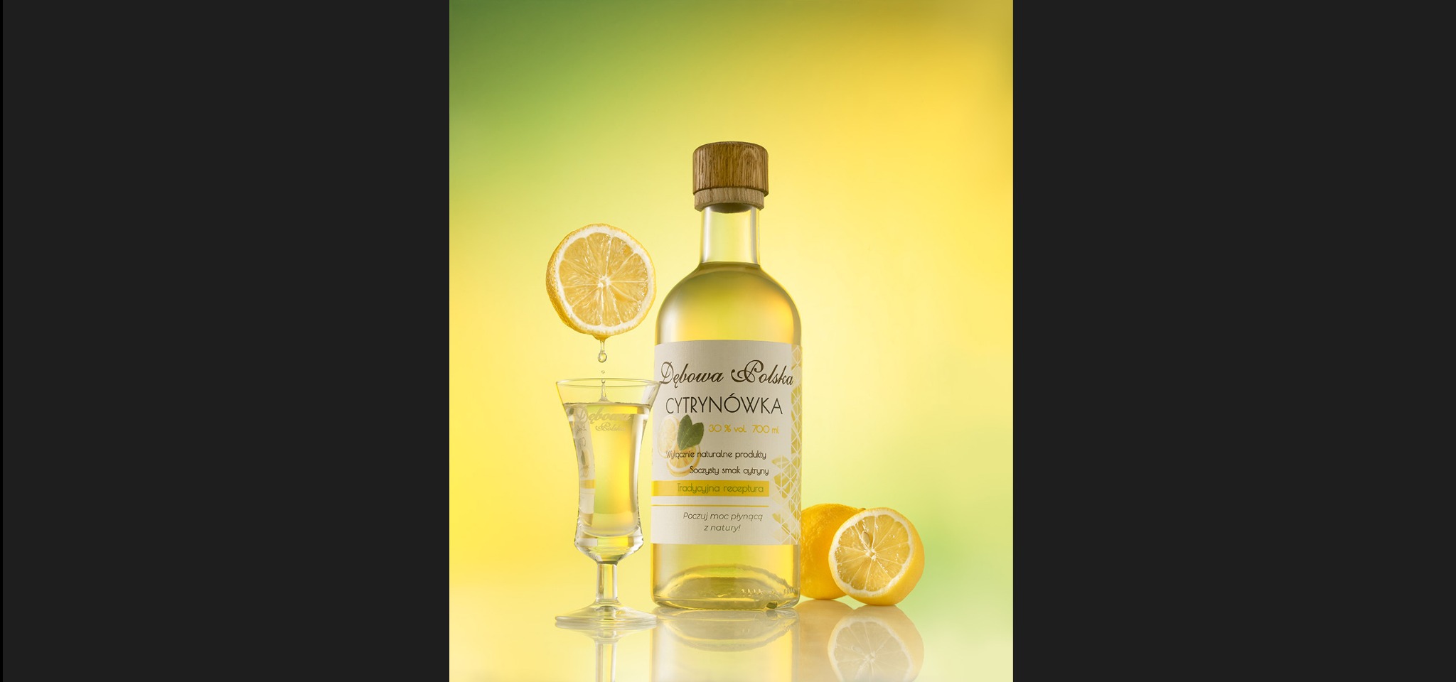 Zdjęcie butelki cytrynówki Dębowa Polska, kieliszka i cytryn na żółto-zielonym tle. Profesjonalna fotografia produktowa z Zielonej Góry, idealna do reklamy.