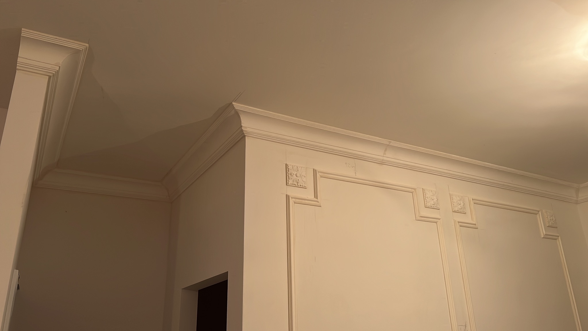 Eleganckie, białe listwy dekoracyjne zdobią ściany i sufit, tworząc klasyczny wystrój wnętrza. Widoczne zdobienia i precyzyjne wykończenie.