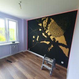 WSZYSTKO ALBO NIC NIKOLA OSIŃSKA - Pokój po malowaniu ścian z unikalnym wzorem w kolorze czarnym i złotym, drabina malarska stoi przy ścianie, widok na okno i grzejnik.