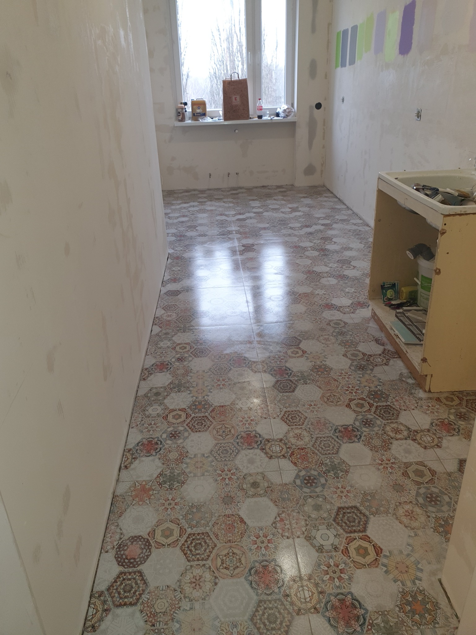 Ukończona podłoga z heksagonalnych płytek w łazience w trakcie remontu. Widoczne ślady po szpachlowaniu ścian i próbki kolorów farb na ścianie.