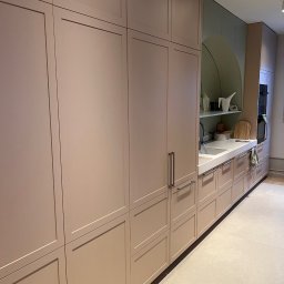 REORGET SPÓŁKA Z OGRANICZONĄ ODPOWIEDZIALNOŚCIĄ - Jasna kuchnia z zabudową na wymiar. Fronty szafek w odcieniach beżu, minimalistyczne uchwyty. Na blacie akcesoria kuchenne i zlew. Nowoczesny design.