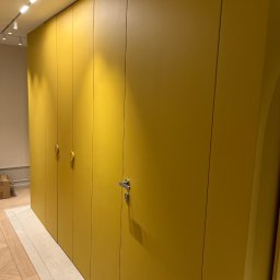 REORGET SPÓŁKA Z OGRANICZONĄ ODPOWIEDZIALNOŚCIĄ - Żółta szafa wnękowa z dyskretnymi uchwytami i drzwiami bez widocznych zawiasów, wkomponowana w nowoczesne wnętrze z oświetleniem punktowym.