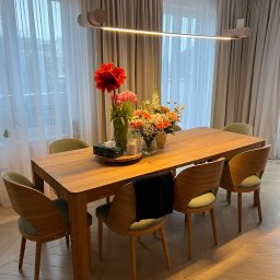 REORGET SPÓŁKA Z OGRANICZONĄ ODPOWIEDZIALNOŚCIĄ - Drewniany stół z krzesłami w jadalni, bukiety kwiatów w wazonach, minimalistyczna lampa. Parkiet ułożony we wzór jodełki. Stonowana kolorystyka, naturalne światło.