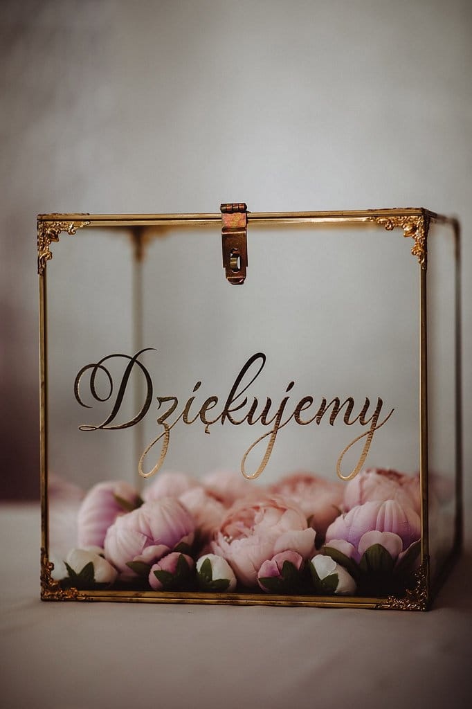 Szklana szkatułka z napisem 'Dziękujemy' i różowymi piwoniami, złote zdobienia, elegancki akcent na przyjęcie weselne, stonowana kolorystyka.