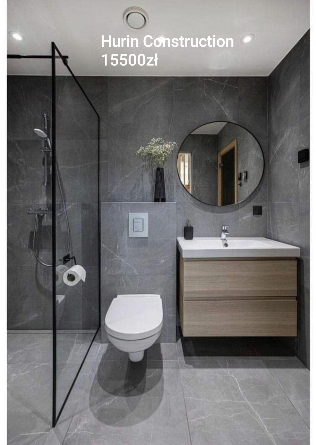 Stylowa, szara łazienka z kabiną prysznicową typu walk-in, okrągłym lustrem, umywalką z drewnianą szafką i wiszącą toaletą. Marmurowa tekstura płytek.