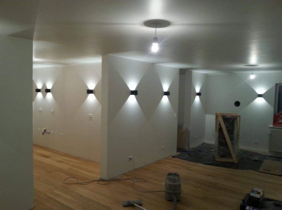 Wykończone wnętrze z drewnianą podłogą i nowoczesnym oświetleniem ściennym, widoczne narzędzia sugerują trwające prace wykończeniowe.