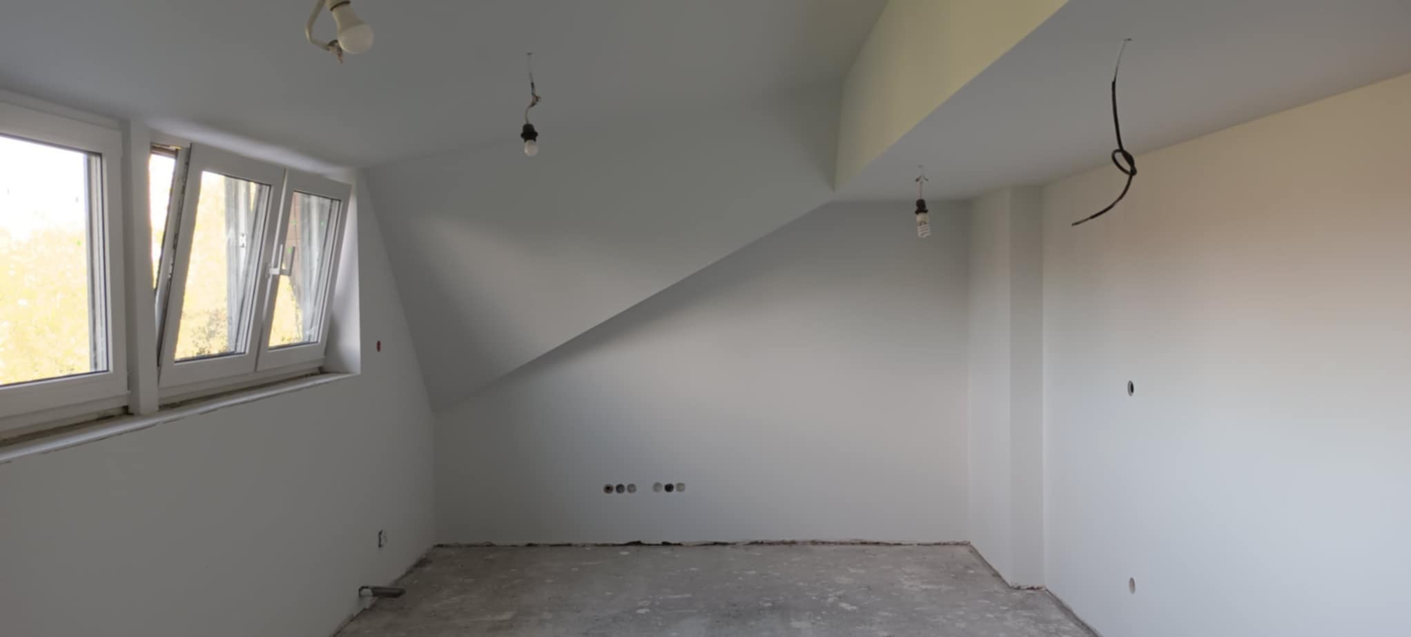 Wnętrze po malowaniu na biało, z oknem i wystającymi kablami. Widoczne ślady po gniazdkach elektrycznych. Podłoga surowa, przed wykończeniem.