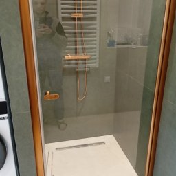 Dmytro Kmetyk - Nowoczesna kabina prysznicowa z elementami w kolorze miedzi, widoczna w łazience po remoncie w Jeleniej Górze. Uwagę zwraca odpływ liniowy i grzejnik drabinkowy.