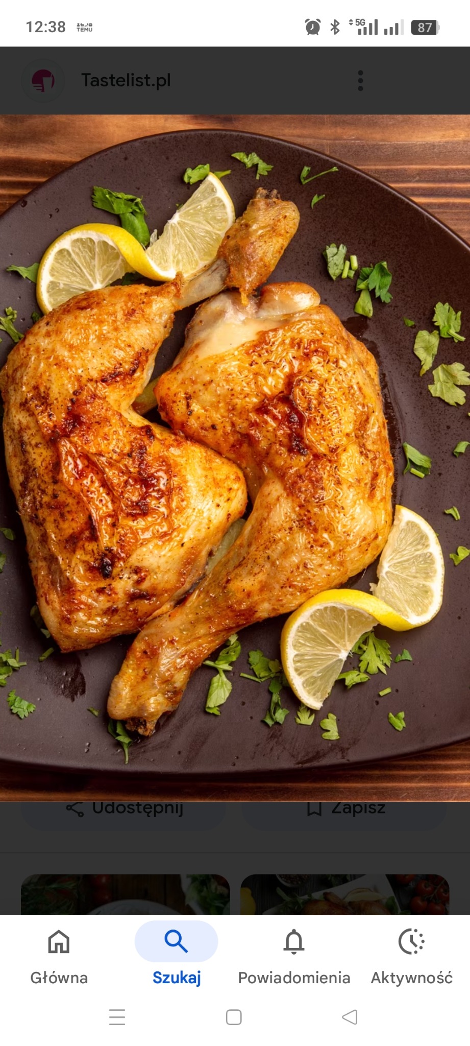 Dwie pieczone ćwiartki kurczaka na brązowym talerzu, udekorowane cytryną i natką pietruszki, na drewnianym stole. Apetyczny detal, ciepłe światło.