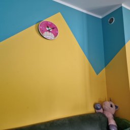 Rydzu - Pomysłowe malowanie ścian w pokoju dziecka: żółte i turkusowe trójkąty. Zegar w kształcie pączka, kalendarz i pluszowy jednorożec dodają uroku.