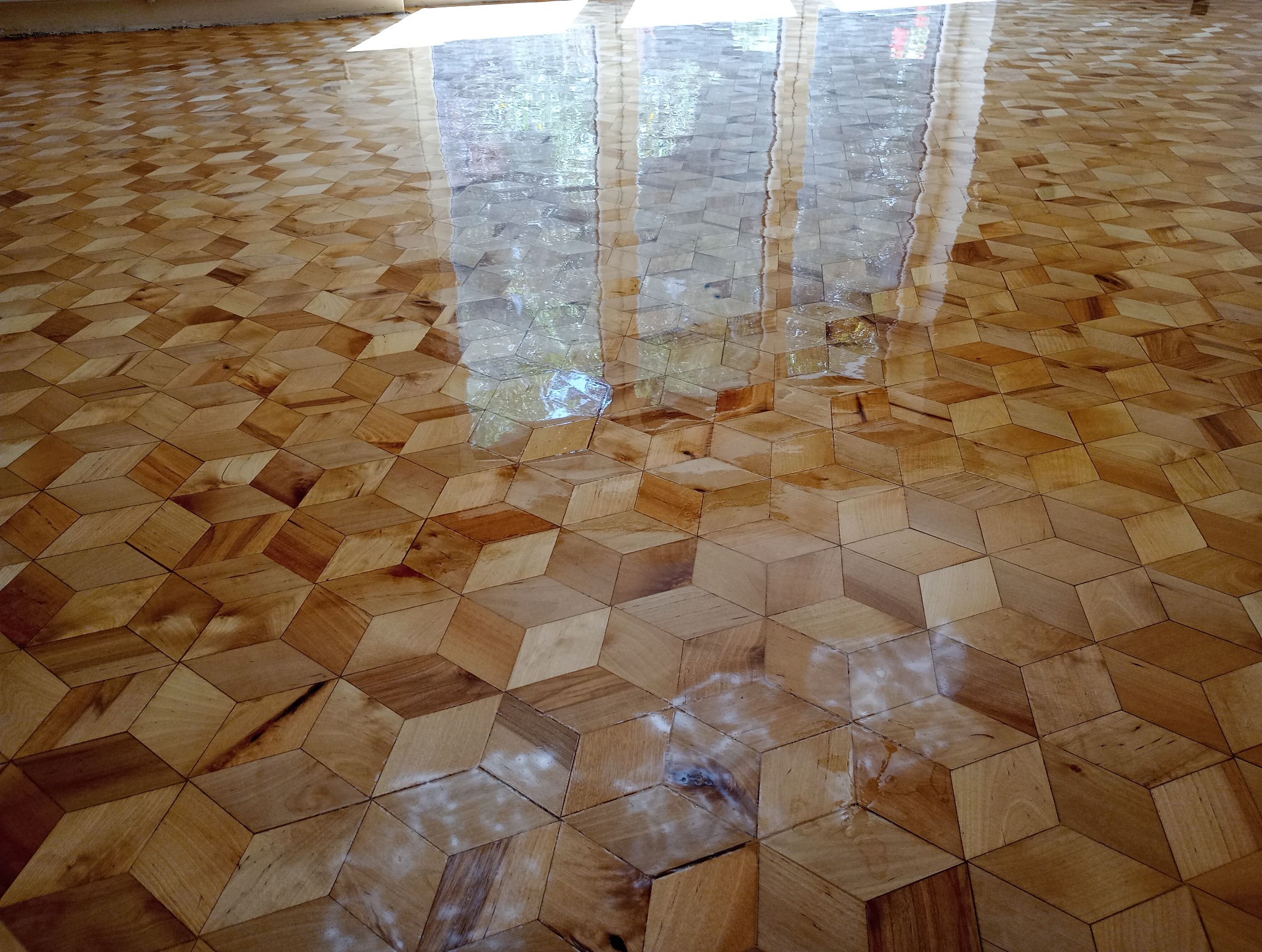 Lakierowana, parkietowa podłoga z geometrycznym wzorem kostek, odbijająca światło okienne. Widoczne niedoskonałości powierzchni i ślady po lakierowaniu.
