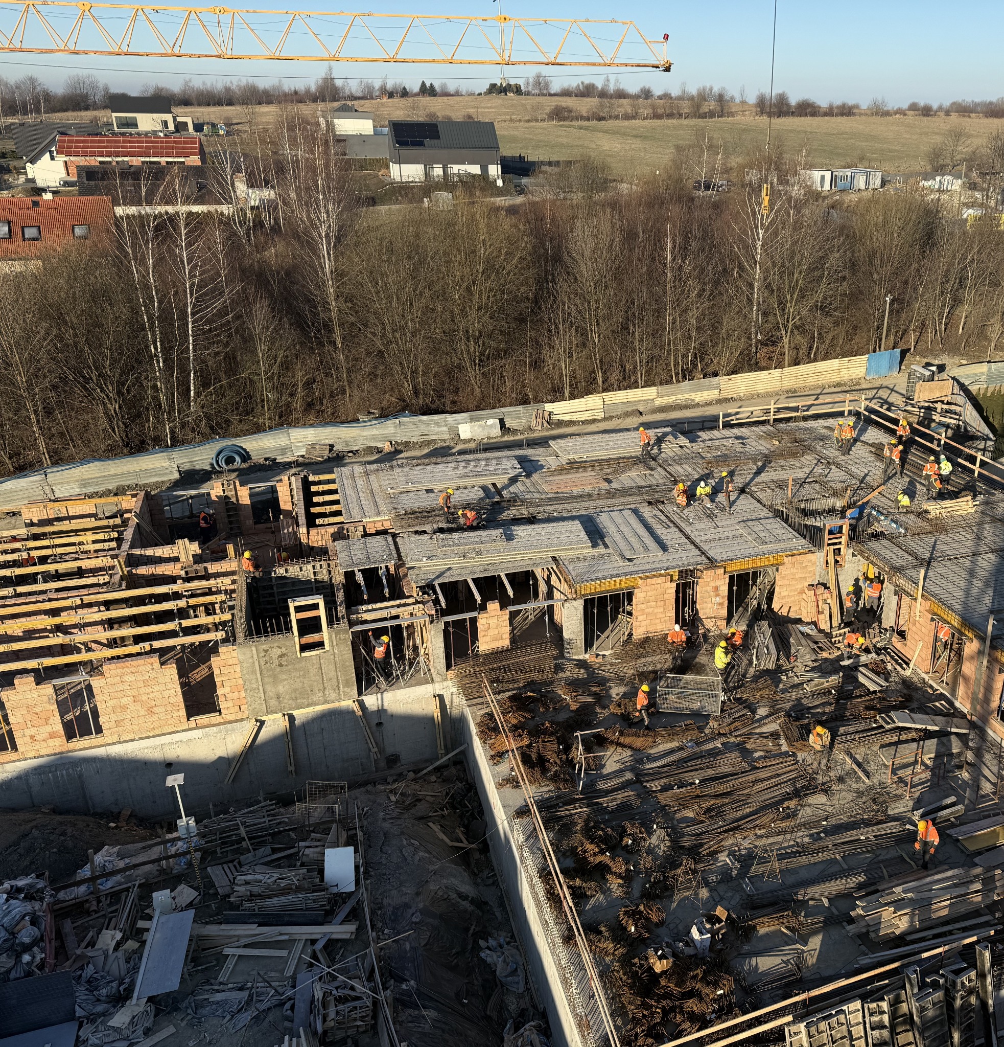Budowa domu wielorodzinnego w trakcie realizacji: widok z góry na zbrojenie stropu, murarzy i dźwig. Budowa w toku, z widocznymi elementami konstrukcyjnymi.
