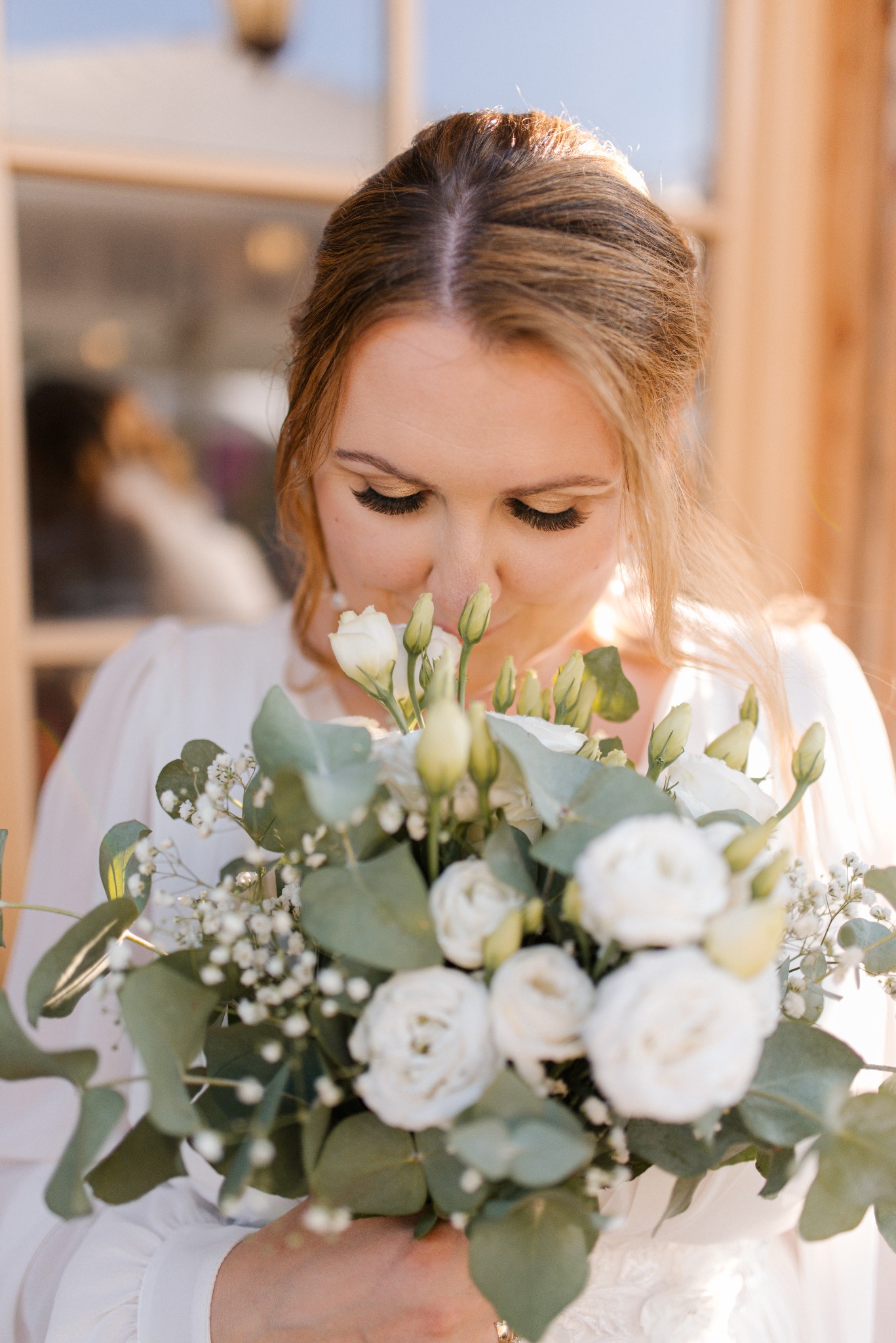 Panna młoda w białej sukni z delikatnym bukietem, pochylona, wdycha zapach kwiatów. Stonowana kolorystyka, miękkie światło podkreślają subtelność chwili.